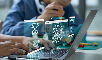 Künstliche Intelligenz Schule: Sollte Künstliche Intelligenz in der Schule unterrichtet werden, wie dieses Symbolfoto hier zeigt, auf dem zwei Kinder zu sehen sind, ein Kind am Laptop und ein anderes mit Werkzeug in der Hand; wie ein Hologramm werden mehrere Fenster von einem Computer-Programm über dem Laptop gezeigt, wobei in dem mittleren Fenster ein Kopf zu sehen ist, der mit Schaltkreisen verbunden ist und statt eines Gehirns ist ein Zahnrad im Kopf und im Zahnrad steht AI, was die Abkürzung von Artificial Intelligence ist, also dem englischen Begriff von Künstliche Intelligenz.